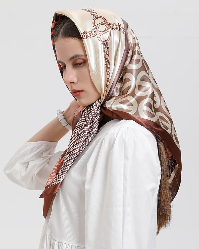 Woman in a white blouse wearing a cream and chocolate silk square printed with golden chains over her hair